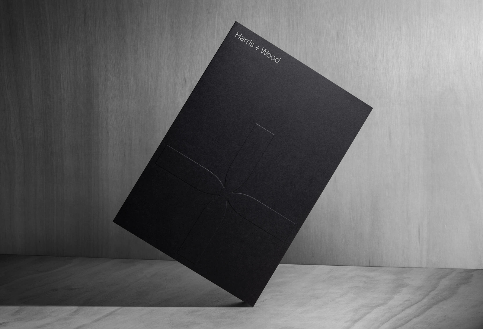 Black Harris + Wood presentation folder with embossed cross-shaped brand mark